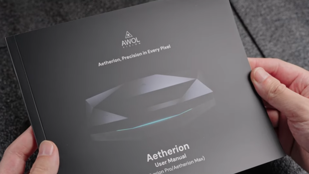A person holds the black user manual for the AWOL Vision Aetherion projector, representing the first step in unboxing and setting up a new home theater system.