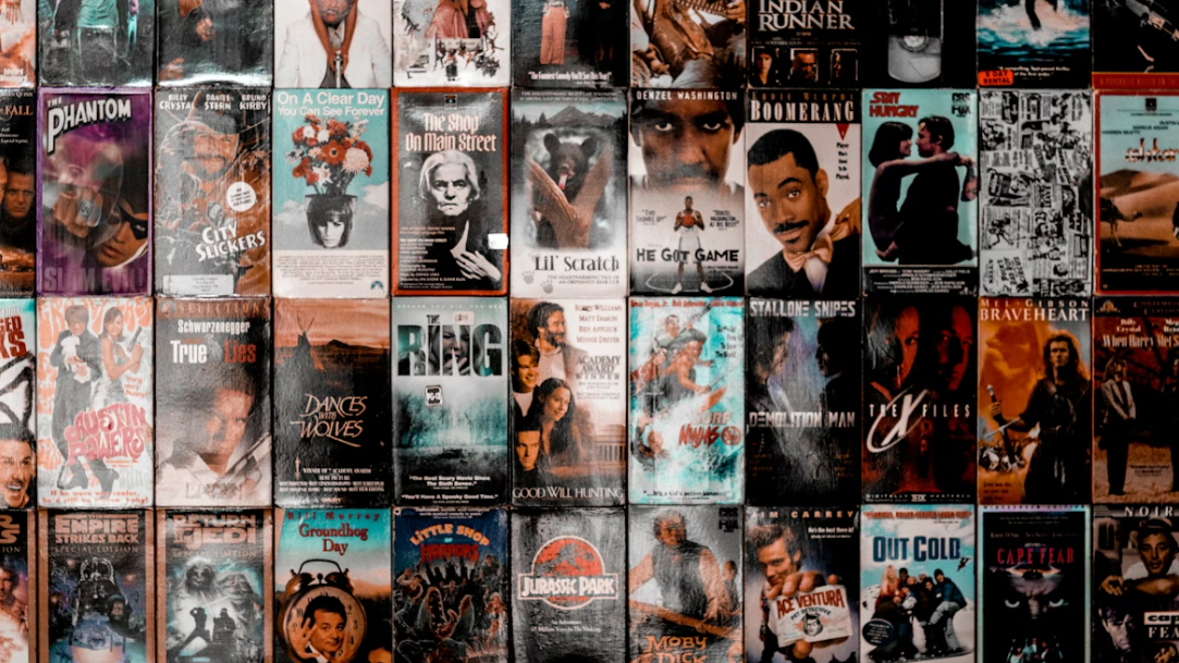 A nostalgic wall display of classic 90s VHS movie covers arranged in a grid, featuring recognizable titles like Jurassic Park, Braveheart, and Groundhog Day.