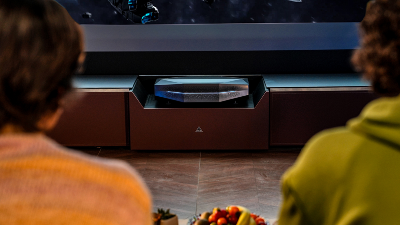 Two people sit in a living room enjoying a cinematic movie experience powered by an AWOL UST projector seamlessly integrated into a dedicated media cabinet.