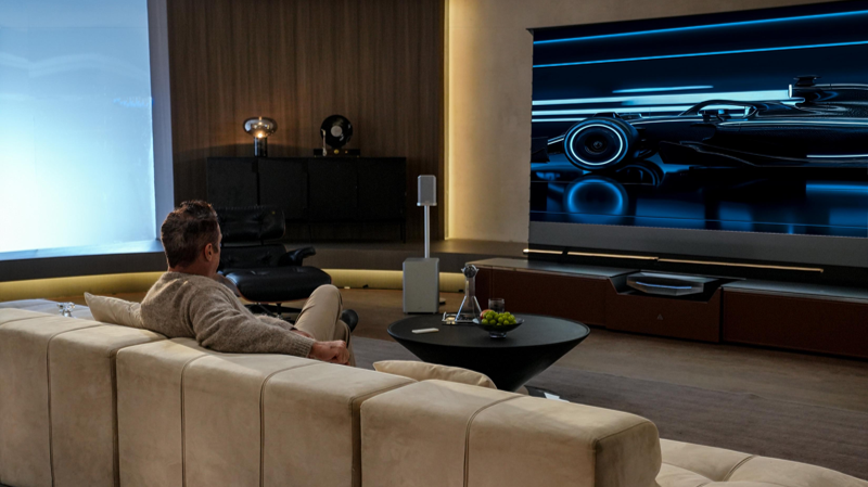 A person sits in a luxurious living room enjoying a massive cinematic display powered by the complete AWOL Aetherion and ThunderBeat audio ecosystem.
