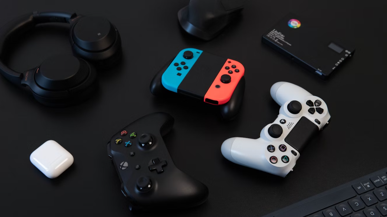 A collection of modern gaming accessories, including Nintendo Switch, Xbox, and PlayStation controllers, laid out on a dark surface.