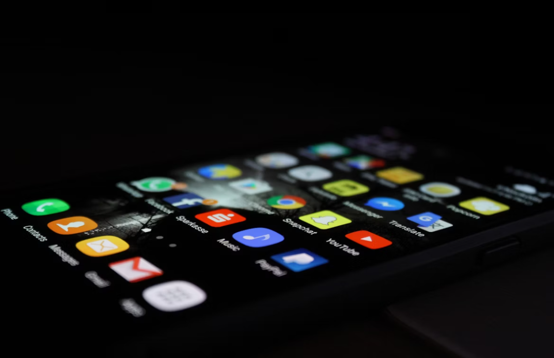 A close-up of a smartphone screen in the dark, showing a grid of various colorful application icons 
