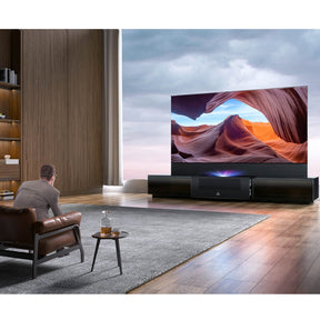 Modern living room featuring AWOL Vision Vanish Laser TV with the LTV-3500 ust laser projector and a motorized rollable screen, displaying a vivid desert landscape.