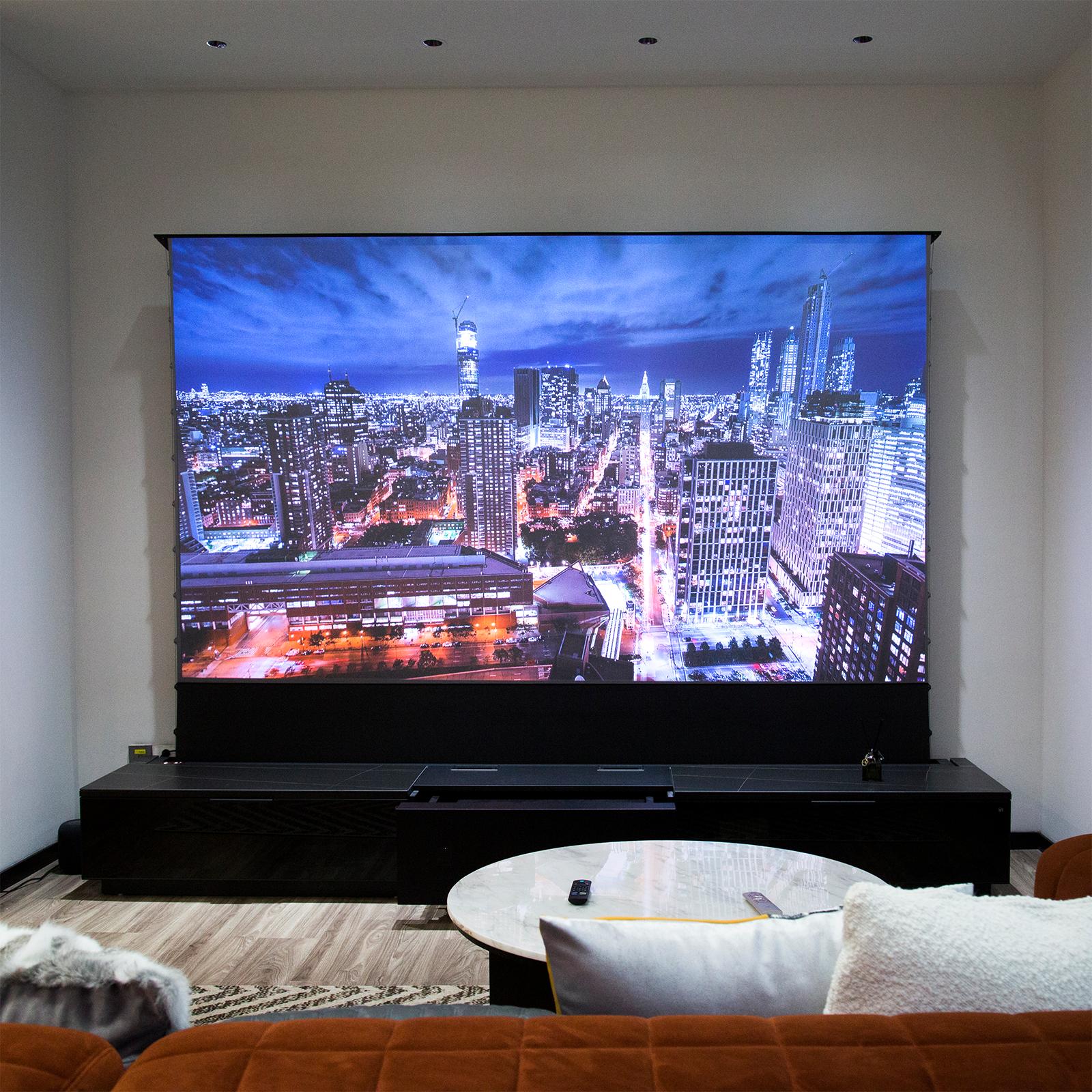 Luxurious living room featuring AWOL Vision LTV-3500 4k ust laser projector, motorized screen, and smart cabinetry displaying vibrant cityscapes for a cinematic experience.